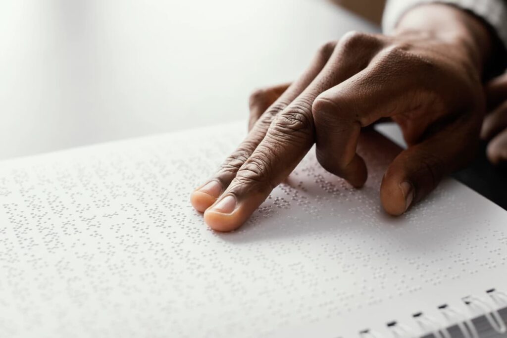 Image from Freepik of a man's hand on a page of braille