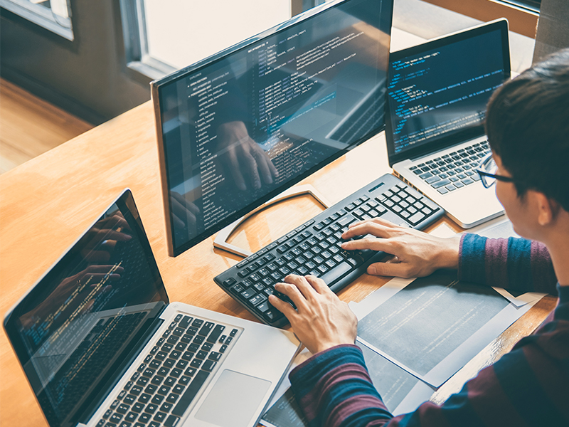 Man typing on a keyboard surrounded by three laptops