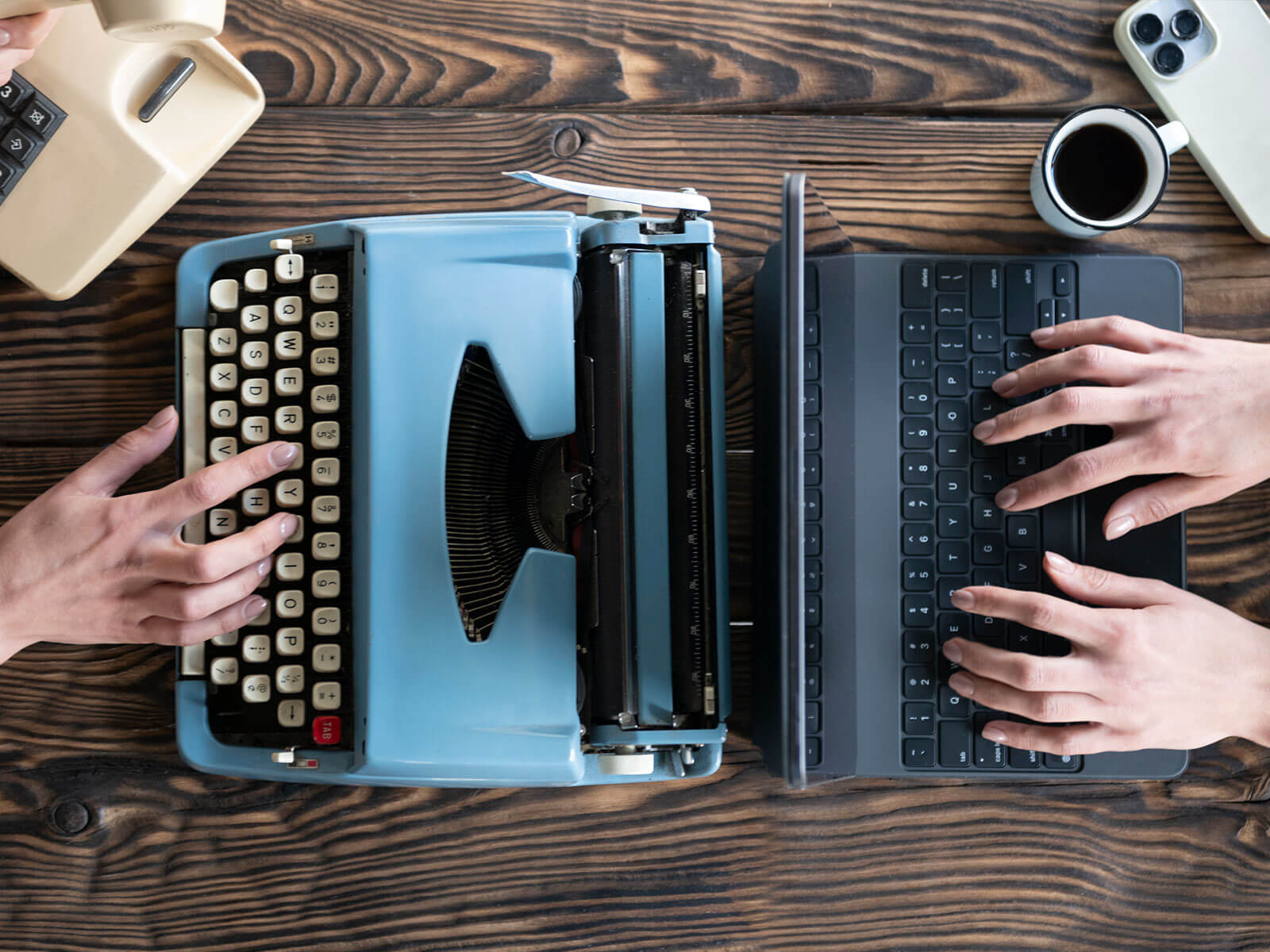 Two people typing, one in an old typewriter and another in a modern laptop