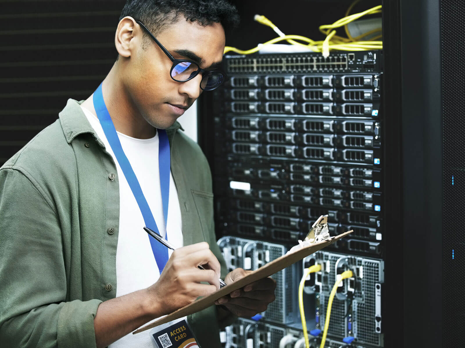 Young individual taking notes while working in a server room, indicating IT infrastructure management