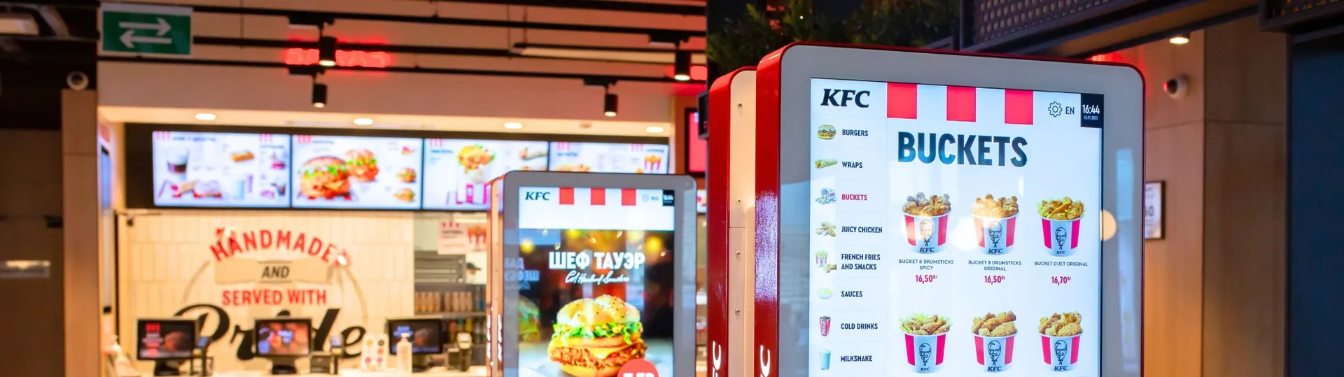 KFC self-service ordering kiosks displaying menu options with buckets, wraps, and pricing