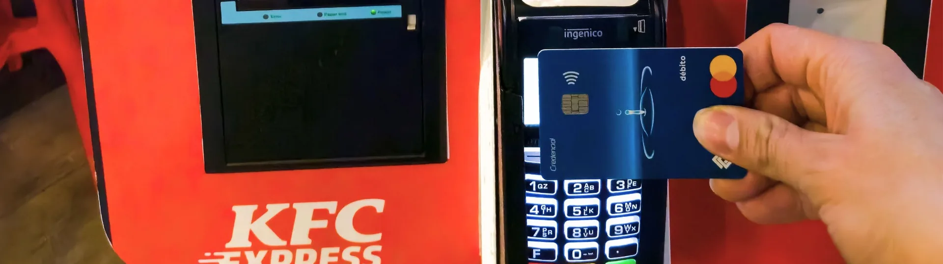 Hand inserting credit card into contactless payment terminal at KFC kiosk