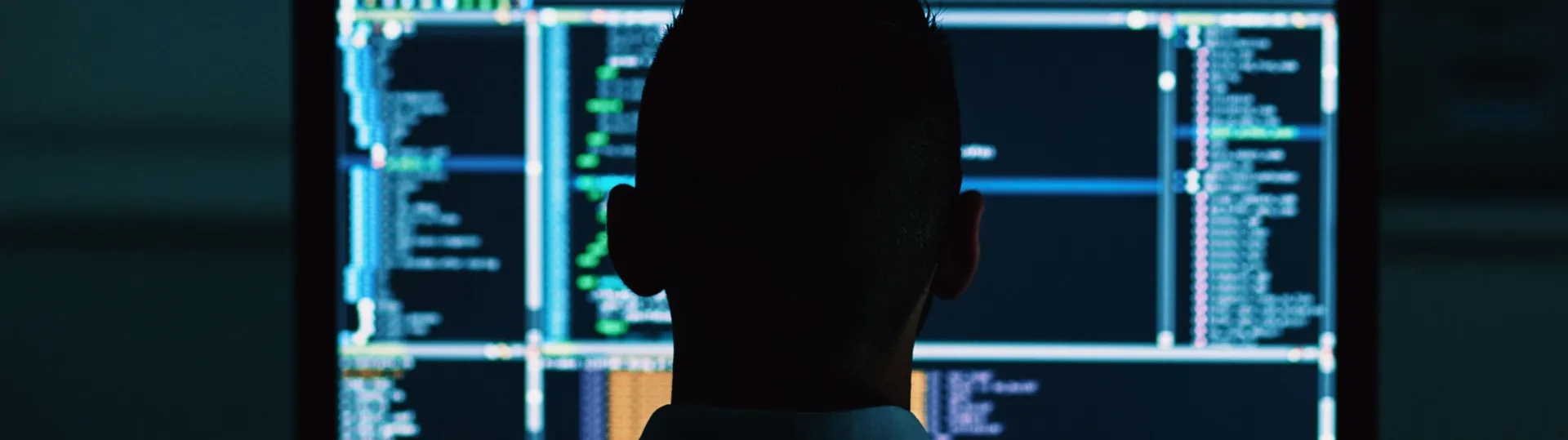 Software analyst reviewing code on multiple monitors in dark environment