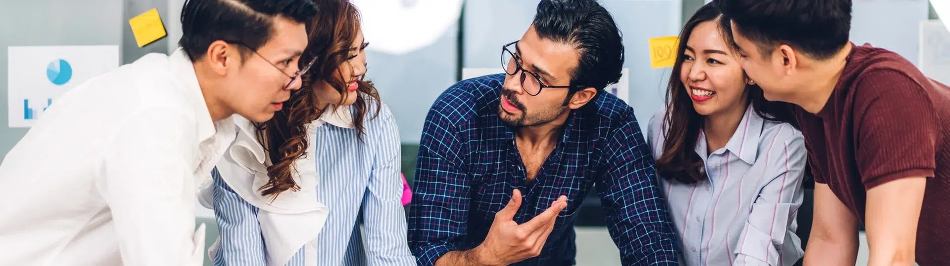 Cross-functional team of five professionals gathered around a laptop reviewing business data and printed reports