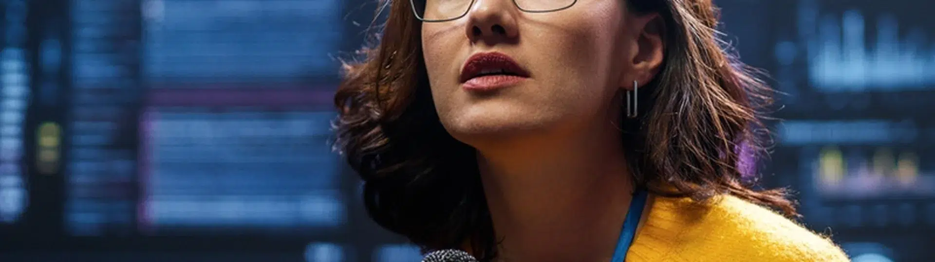 Female tech professional speaking with a microphone in front of large data analytics dashboards at a conference