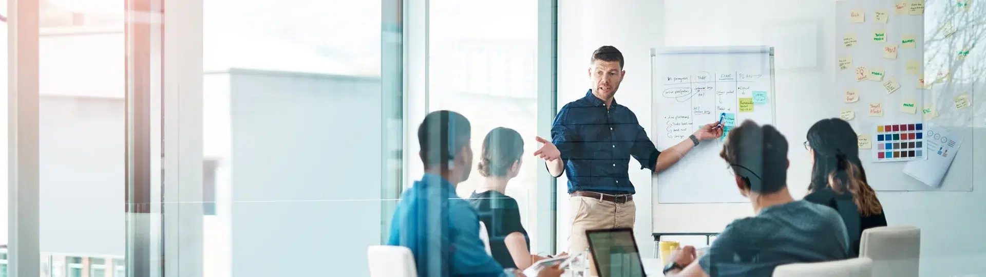 Team meeting in a modern office with a presenter at a whiteboard covered in sticky notes and strategy frameworks