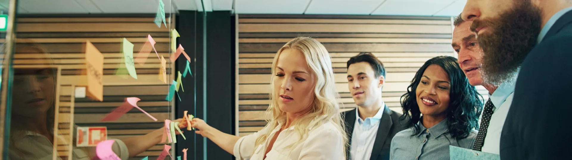 Business team brainstorming and reviewing sticky notes on a glass wall during a strategy session