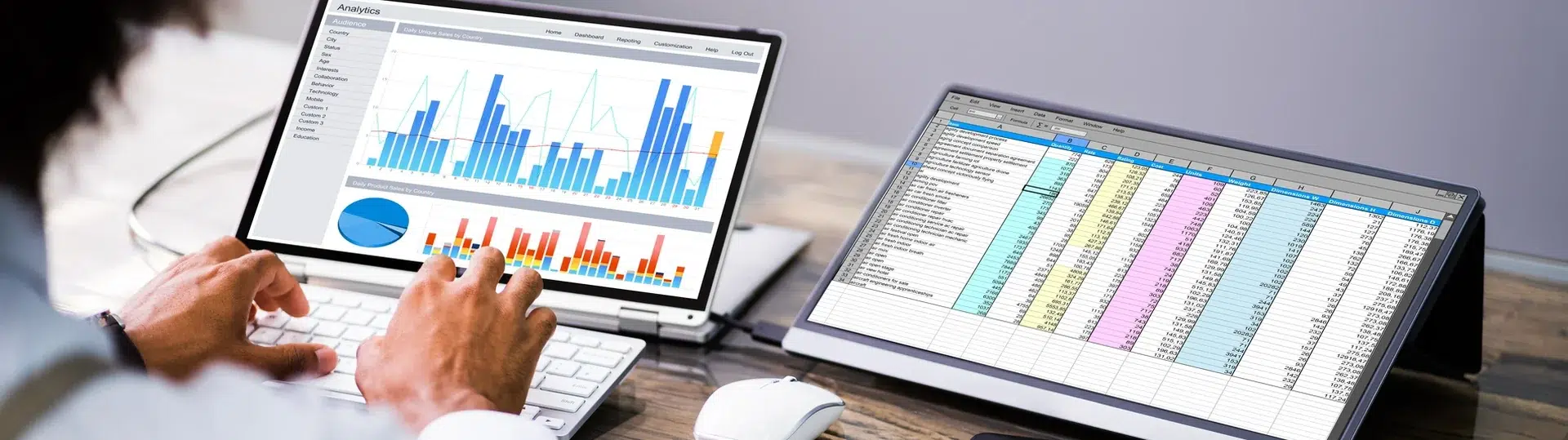 Business analyst reviewing analytics dashboard and spreadsheet data on dual monitors at a desk