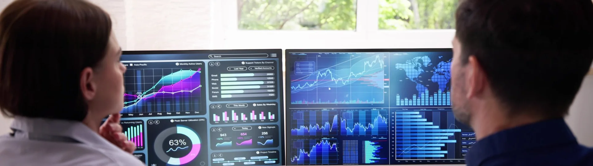 Two business analysts reviewing data dashboards displayed across dual monitors