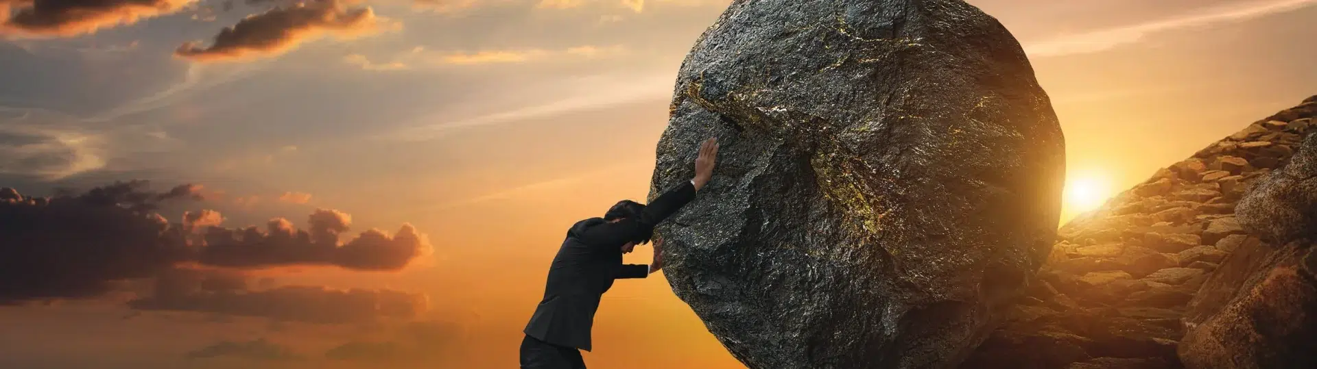 Businessman pushing a boulder uphill at sunset, symbolizing the challenge of scaling software engineering teams under pressure