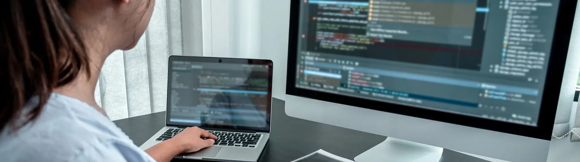 Developer working at a desk with dual monitors displaying code editor and development tools