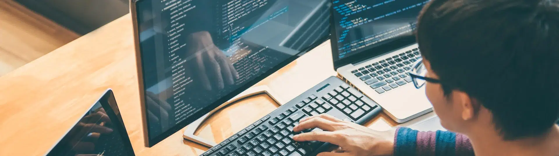 Developer writing code at multiple screens with overhead perspective showing full workstation setup