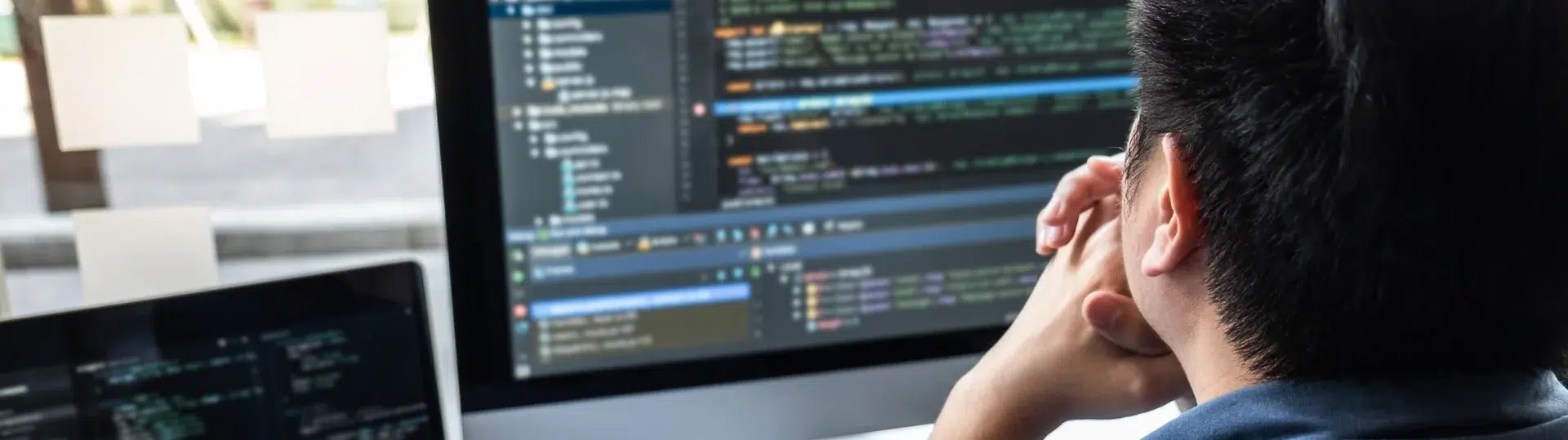Developer leaning forward studying code on dual screens in a focused debugging session