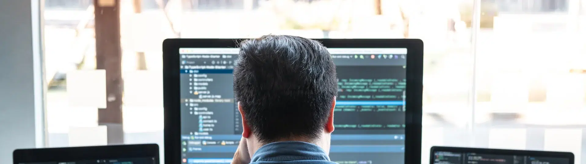 Developer focused on multi-monitor coding setup analyzing complex systems in a professional environment