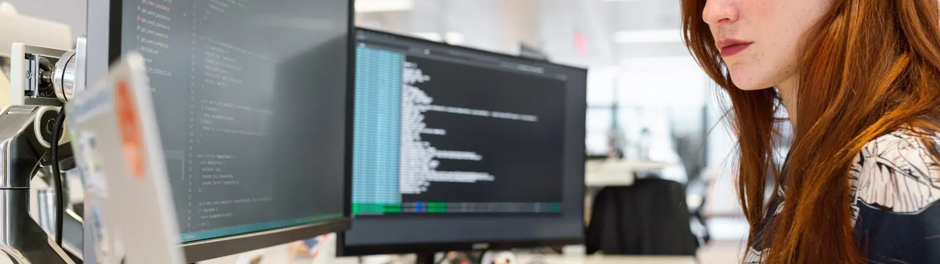 Female developer focused on reviewing code across multiple monitors at a developer workstation