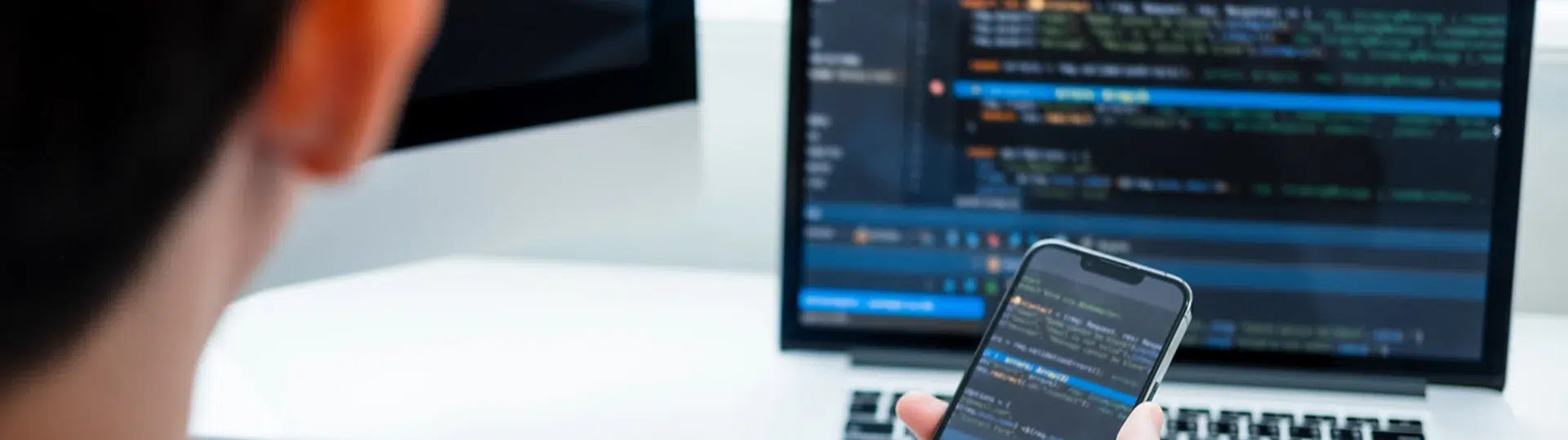 Developer reviewing code across a laptop and mobile device in a modern workspace
