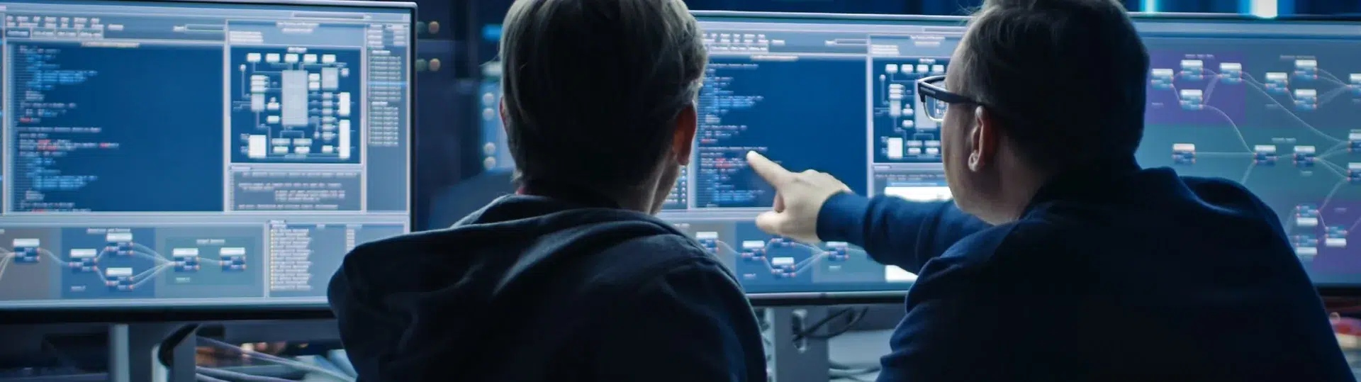 Two developers at multi-monitor workstation analyzing system architecture and pipeline diagrams