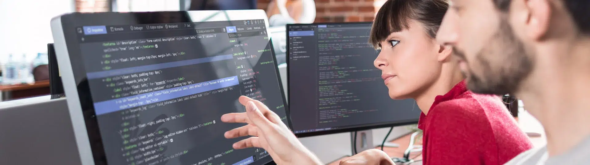 Two software developers collaborating on a code review at dual monitors in a modern office