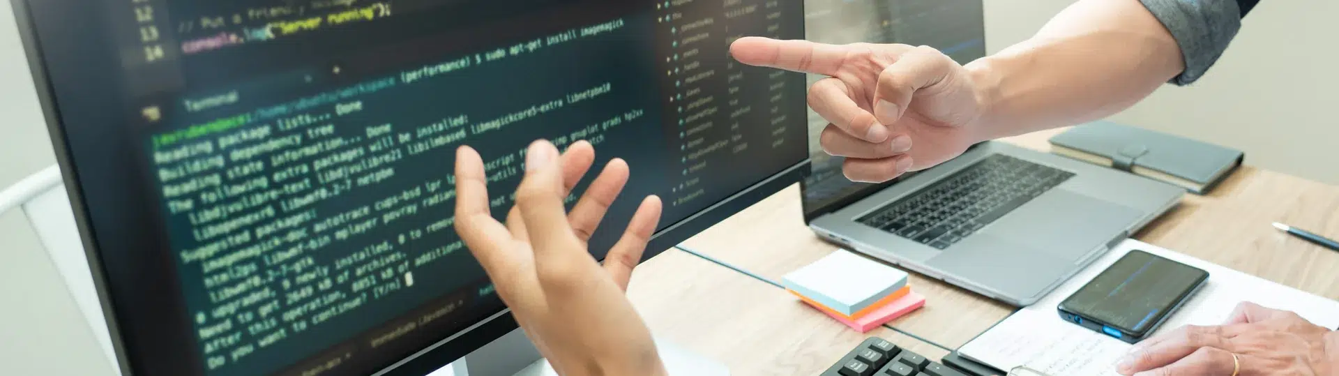 Two developers reviewing terminal code output on a large monitor at a workstation