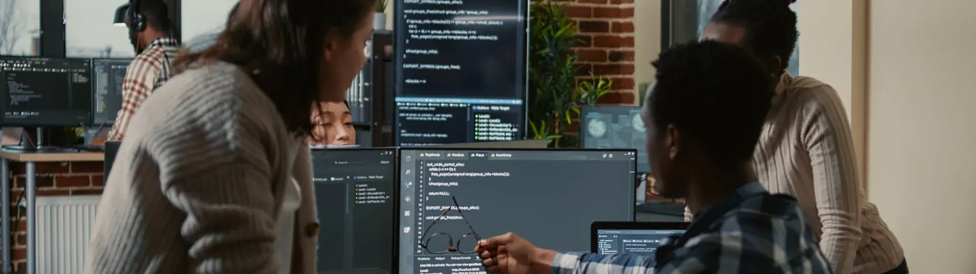 Diverse software development team collaborating around multiple monitors reviewing code together