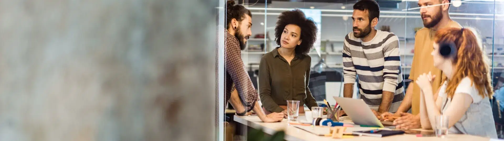 Diverse software development team collaborating around a table in a modern glass-walled office