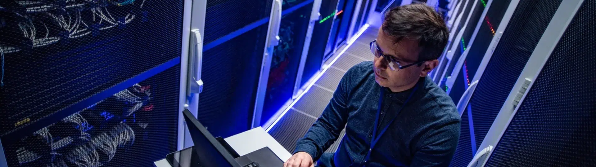 IT engineer working on laptop in a blue-lit server room data center