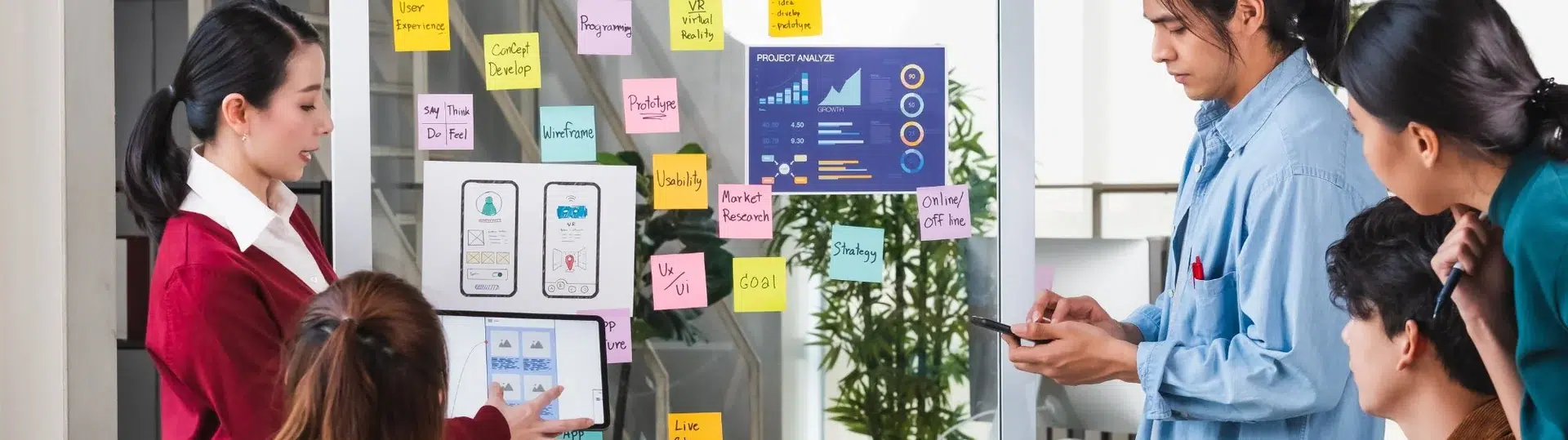 Mobile app development team presenting UX/UI strategy on a glass board covered with sticky notes and wireframes