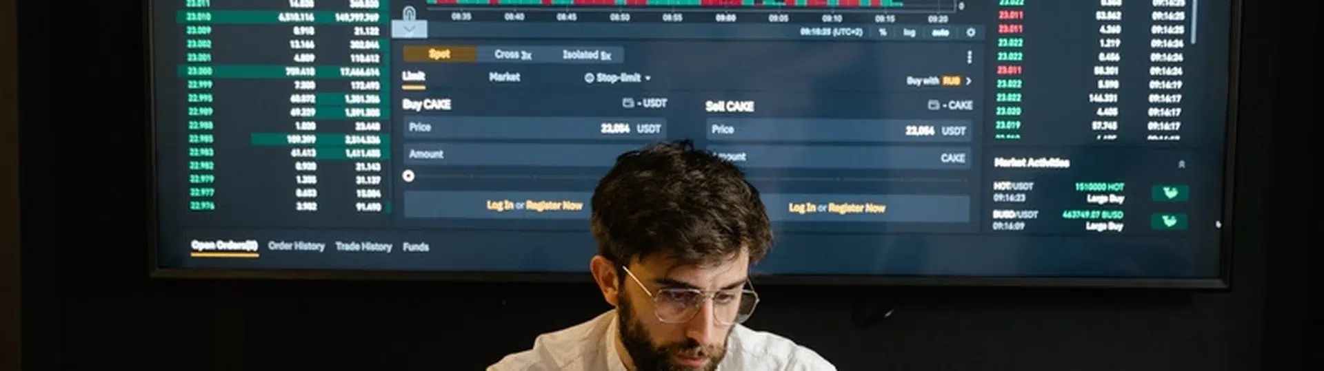 Professional analyzing data on a laptop with a large trading and analytics dashboard displayed on screen