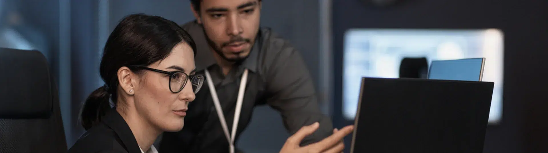 Two professionals collaboratively reviewing work on a computer screen in a dark technology office setting