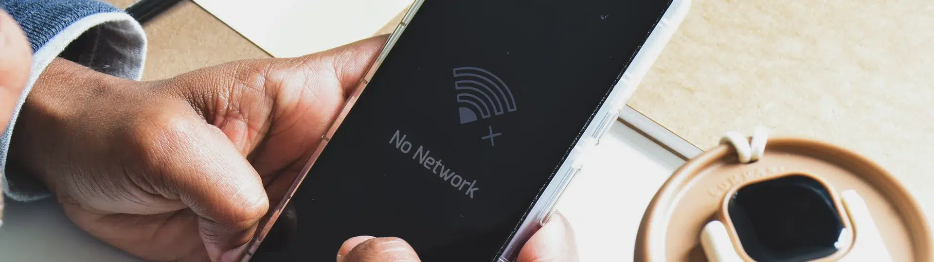 Hands holding a smartphone displaying a No Network error message illustrating IoT connectivity challenges