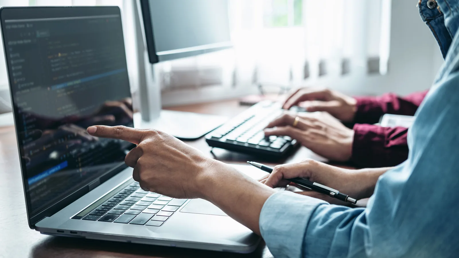 Two people pointing at a laptop screen during a working session