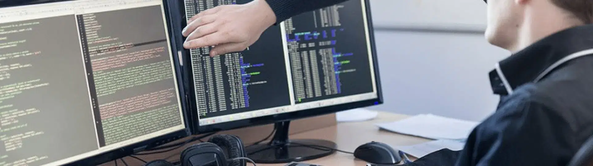 Software developer working with dual monitors displaying application code