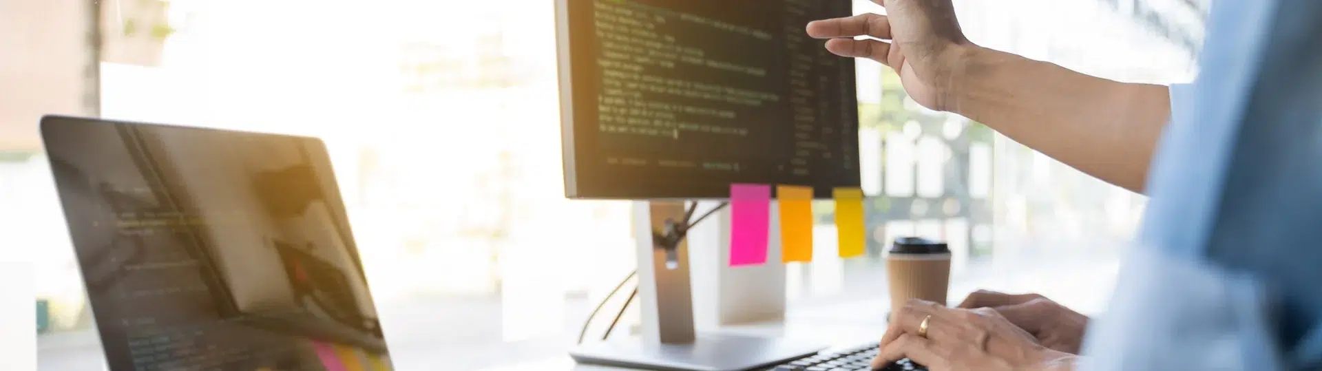 Software developers reviewing code on dual screens in a bright office workspace