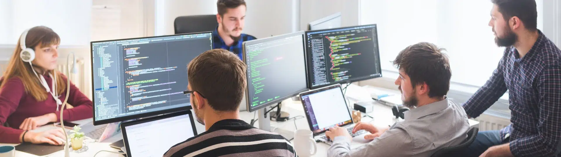 Software development team collaborating at workstations with code visible on multiple monitors
