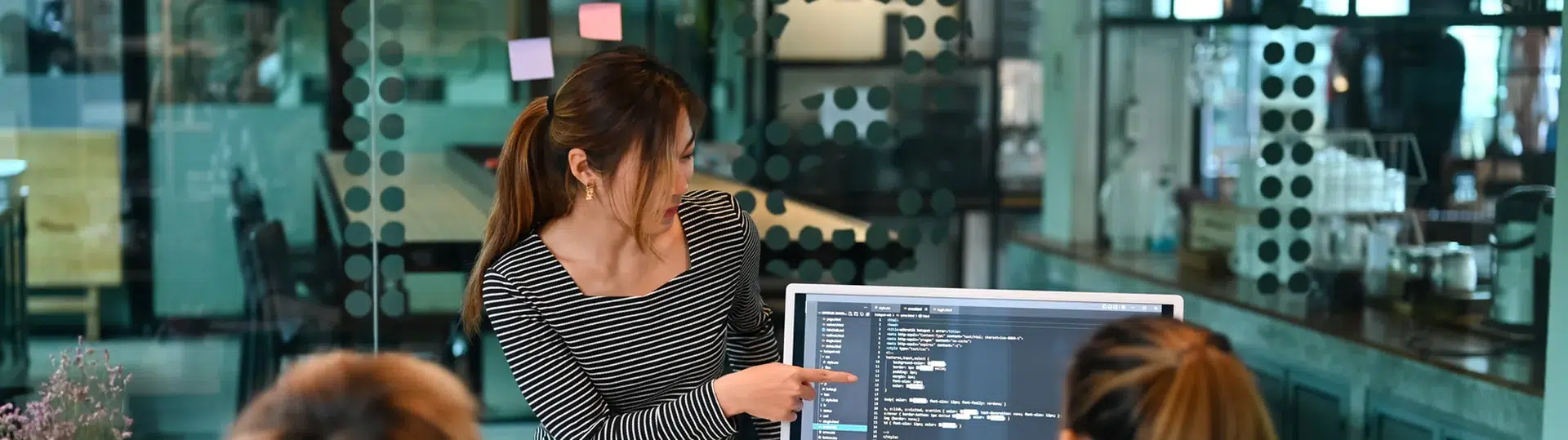 Software engineers collaborating on code review at a desktop monitor in a modern office environment