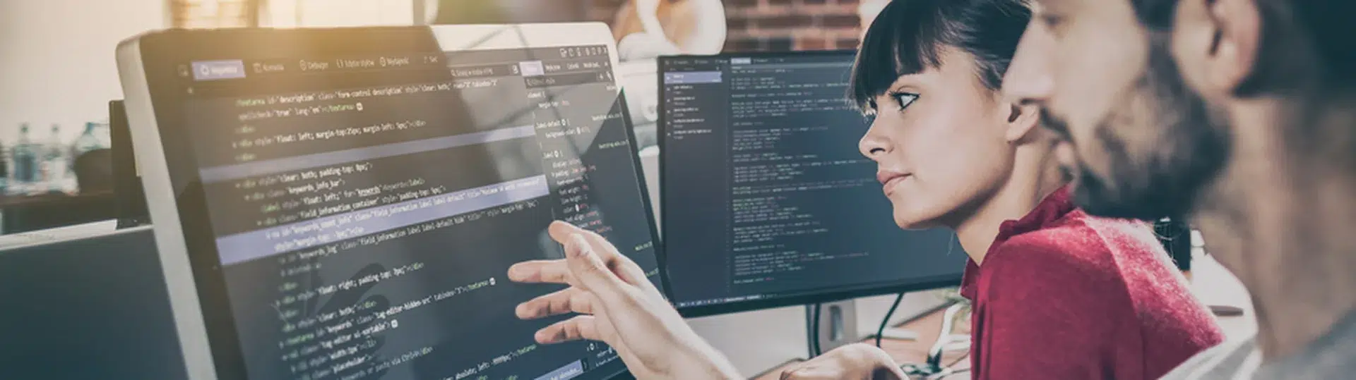 Two software developers collaborating on a code review at a desktop monitor in an open office