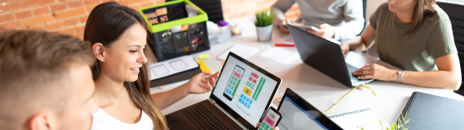 Web development team collaborating around laptops reviewing UI wireframes and app design mockups